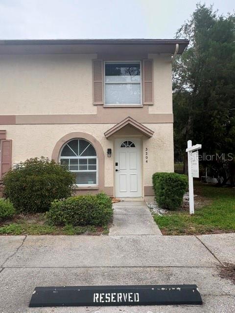 A two-story tan townhouse features a white front door and a reserved parking space — 3204 BRIGADOON DRIVE, CLEARWATER, FL