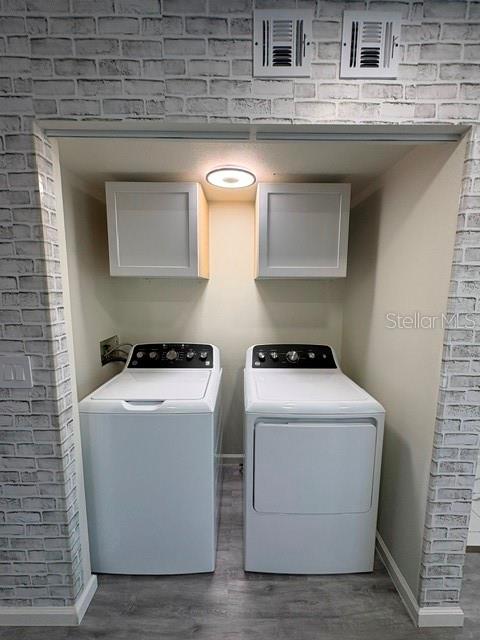 A laundry closet features a white washer and dryer beneath two cabinets against brick-patterned wallpaper — 3204 BRIGADOON DRIVE, CLEARWATER, FL