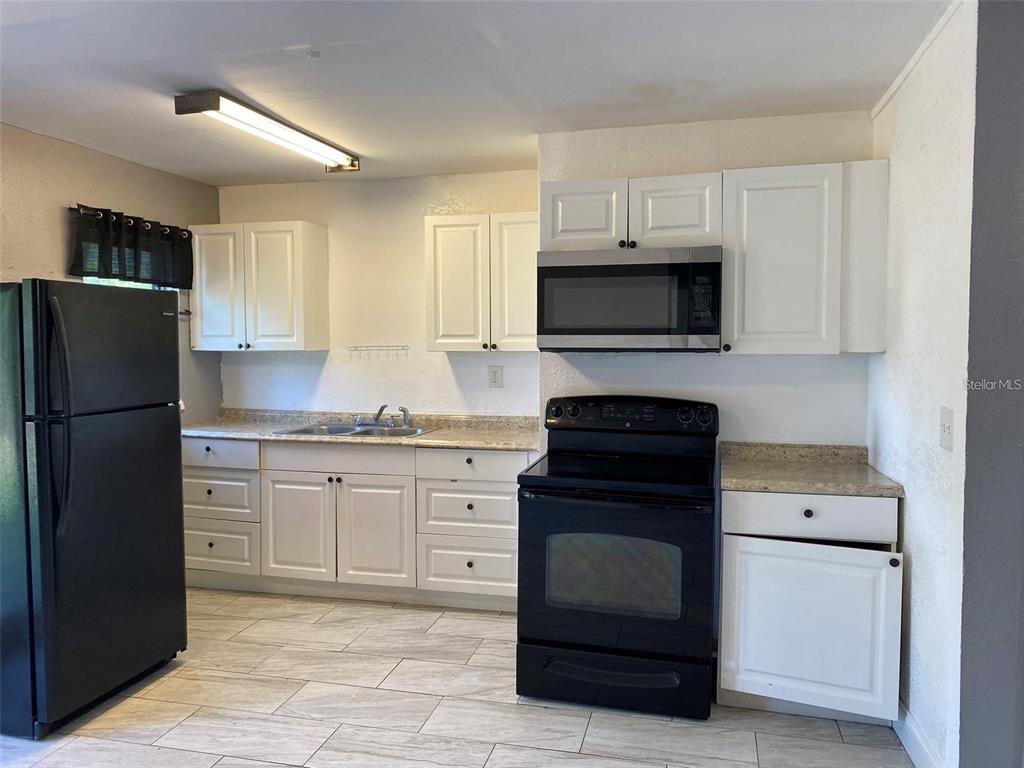 A kitchen features white cabinets, black appliances, a speckled countertop, and light-colored tile flooring — 49 ORANGE PARK BOULEVARD, LAKE WALES, FL