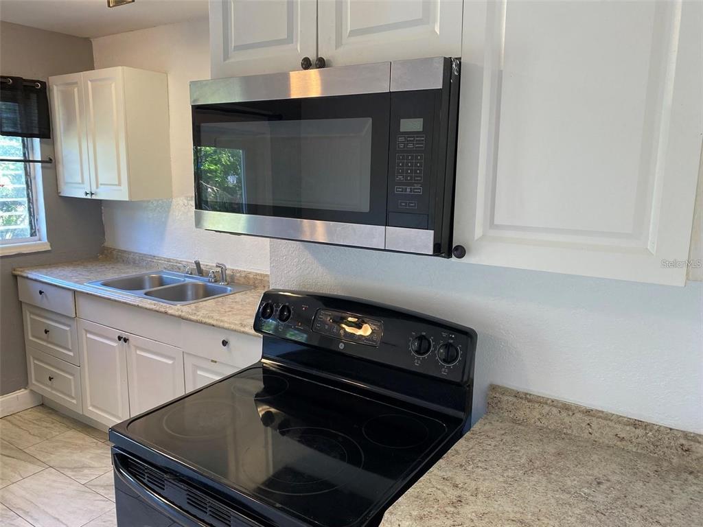 A kitchen features white cabinets, a black electric stove, a microwave, and a double sink — 49 ORANGE PARK BOULEVARD, LAKE WALES, FL