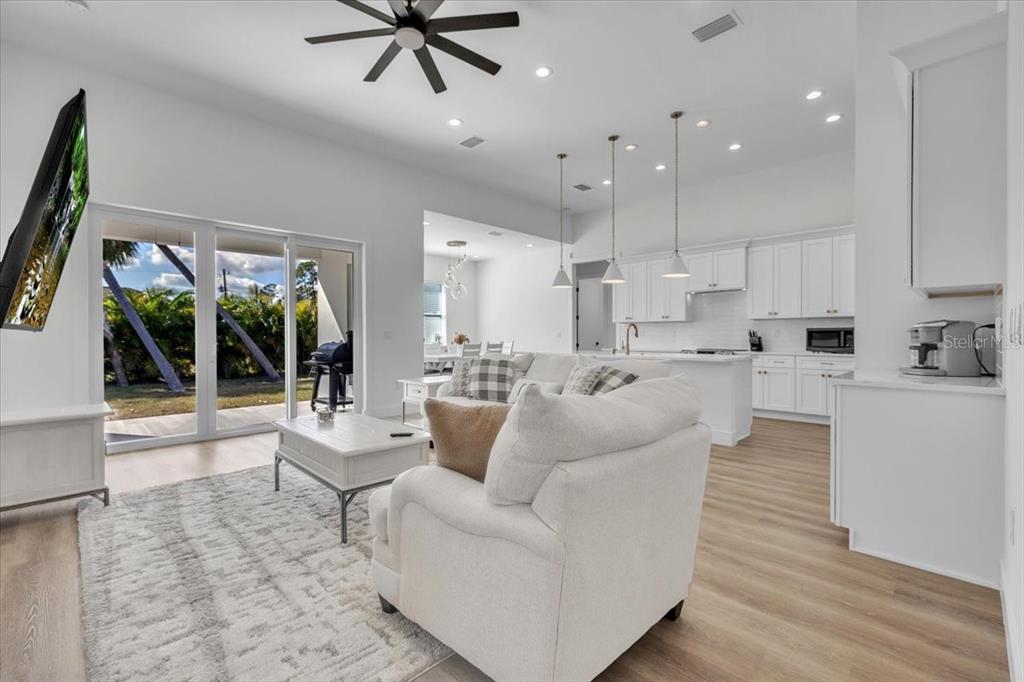 A bright, open-concept living room and kitchen featuring white cabinetry, light wood flooring, and patio access — 3083 JEANNIN DRIVE, NORTH PORT, FL