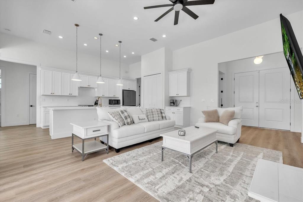 A bright, open-concept living room and kitchen featuring white cabinetry, light wood floors, and neutral furniture — 3083 JEANNIN DRIVE, NORTH PORT, FL