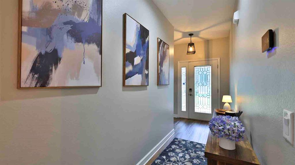A hallway features three abstract paintings, a wooden console table with flowers, and a front door — 741 MYSTIC OAKS LANE, DELAND, FL