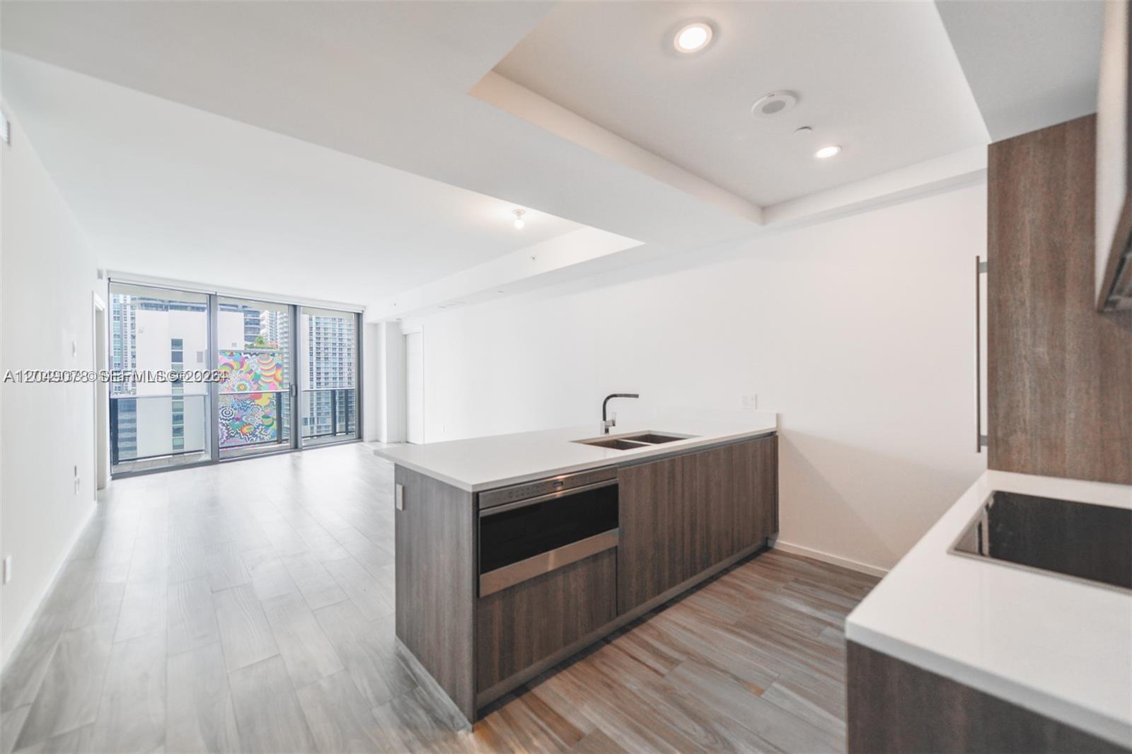 A modern kitchen with a wood-toned island and white countertops overlooks an open living area — 801 S Miami Ave # 1702, Miami FL 33130, MIAMI, FL