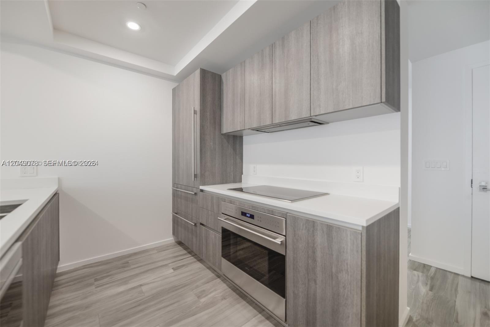 A modern kitchen features gray wood-grain cabinetry, stainless steel appliances, and white countertops — 801 S Miami Ave # 1702, Miami FL 33130, MIAMI, FL