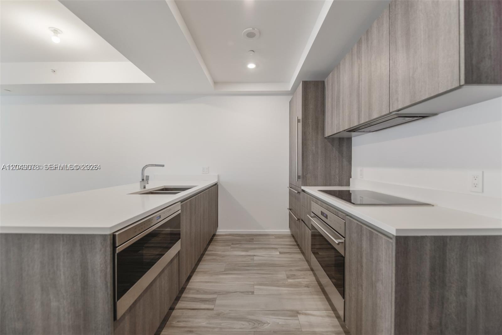 A modern kitchen features wood-grain cabinetry, white countertops, and stainless steel appliances — 801 S Miami Ave # 1702, Miami FL 33130, MIAMI, FL