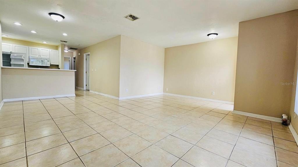 An open-concept living area features light-colored tile flooring and a kitchen with white cabinets — 3026 SANTA BARBARA BOULEVARD, CAPE CORAL, FL
