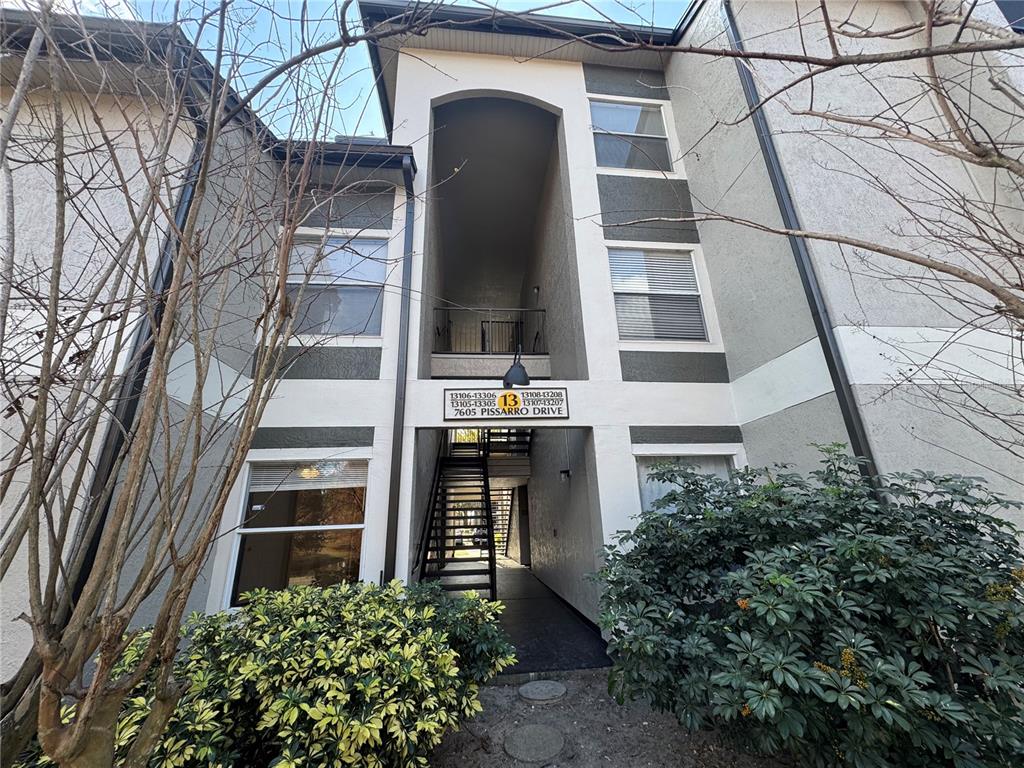 The exterior of a multi-story apartment building features a central stairwell and unit number signage — 7605 PISSARRO DRIVE UNIT 13108, ORLANDO, FL