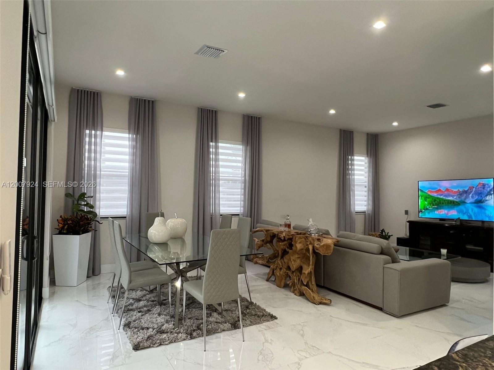 A modern open-concept living and dining area features marble floors, gray furniture, and large windows — 8253 NW 47th Ln, Doral FL 33166, DORAL, FL