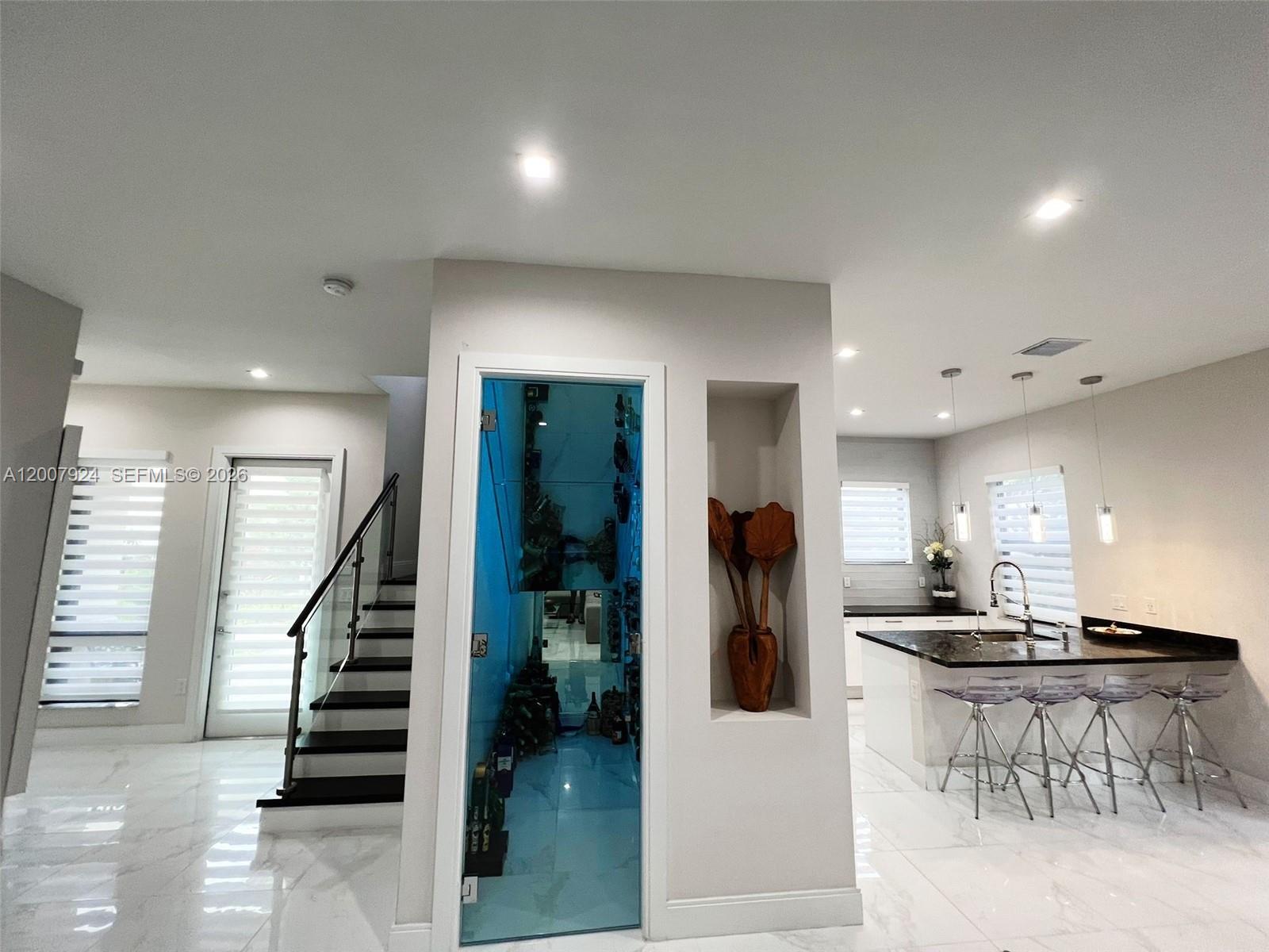 A modern kitchen features a glass-enclosed wine cellar, a breakfast bar, and a staircase — 8253 NW 47th Ln, Doral FL 33166, DORAL, FL