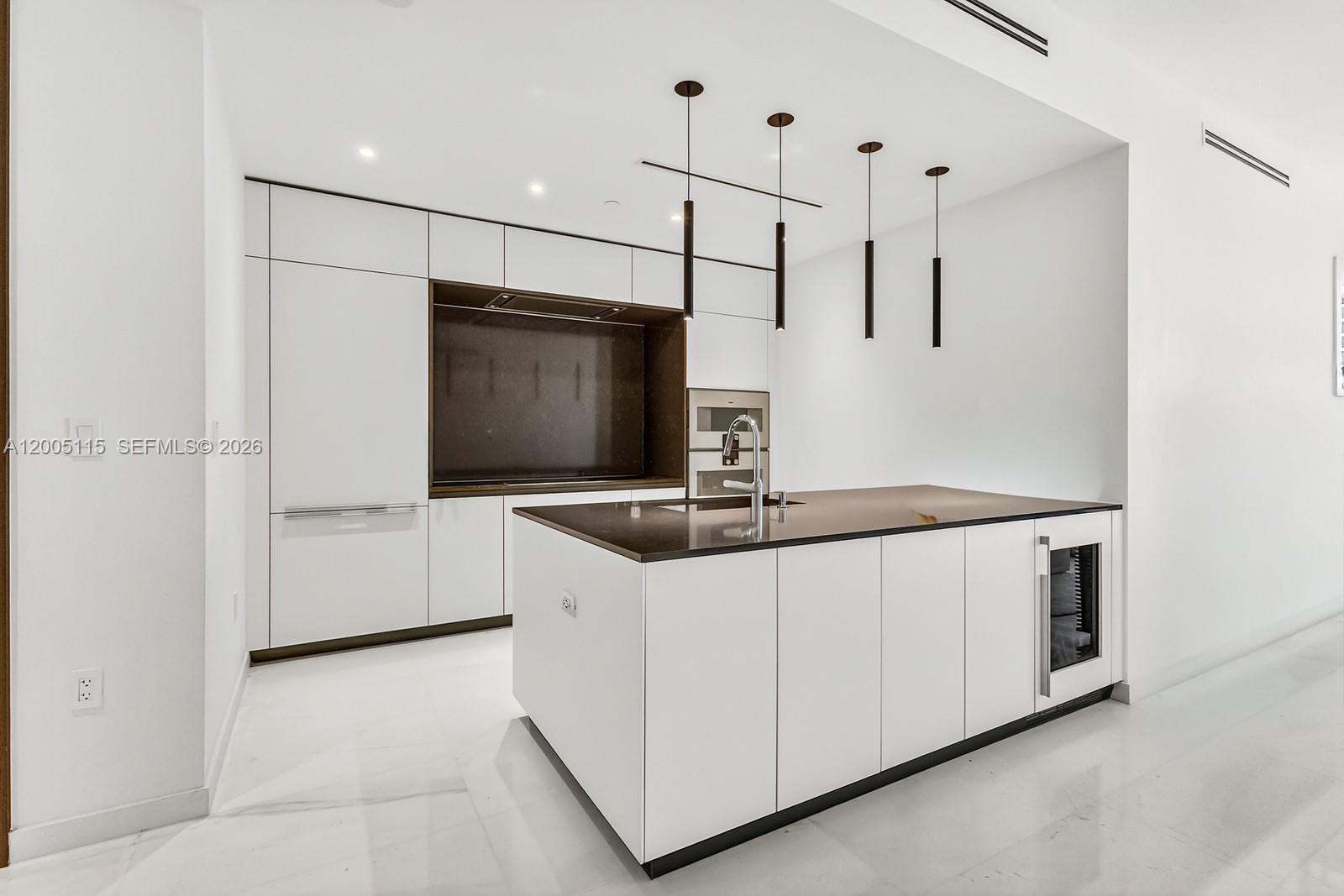 A modern kitchen features white cabinetry, a dark countertop island, and four hanging pendant lights — 300 Biscayne Blvd Way # 1002, Miami FL 33131, MIAMI, FL