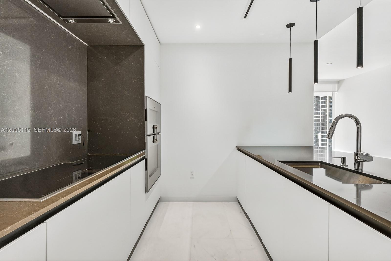 A modern galley kitchen features white cabinetry, dark stone countertops, and minimalist pendant lighting — 300 Biscayne Blvd Way # 1002, Miami FL 33131, MIAMI, FL