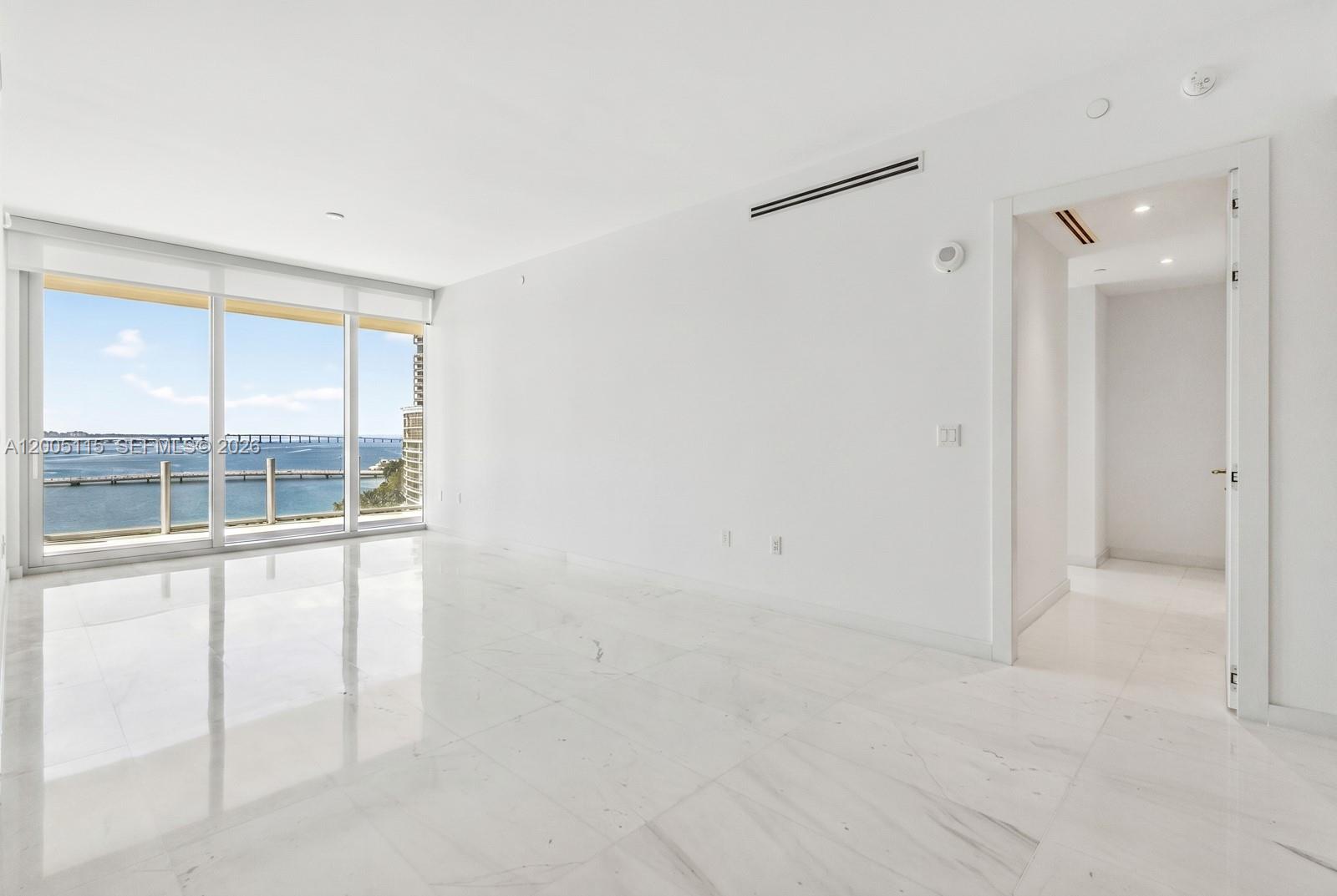 A bright, empty room features white marble flooring, minimalist walls, and floor-to-ceiling windows overlooking water — 300 Biscayne Blvd Way # 1002, Miami FL 33131, MIAMI, FL
