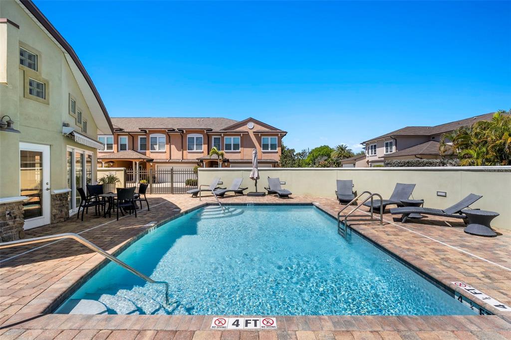 A rectangular swimming pool with a brick deck and lounge chairs sits outside a building — 771 DATE PALM LANE, ST PETERSBURG, FL