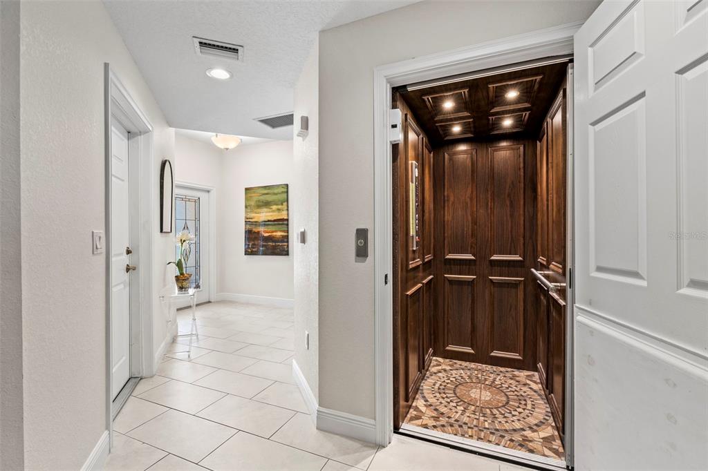 A hallway features light tile flooring, a white door, and an open residential wood-paneled elevator — 771 DATE PALM LANE, ST PETERSBURG, FL