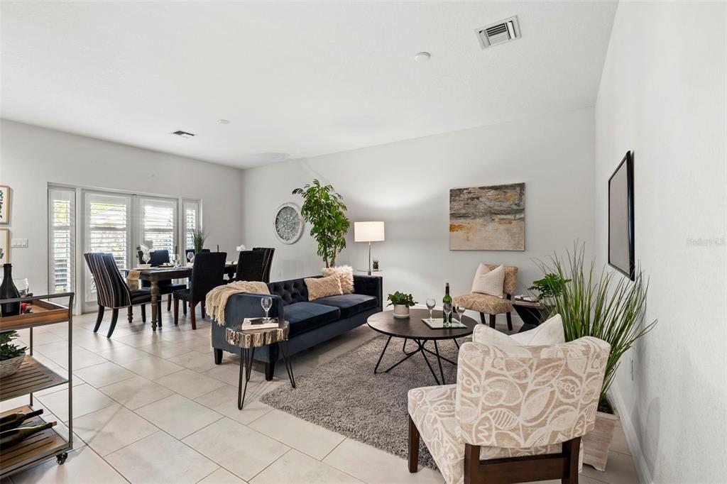 A living room with a blue sofa, patterned armchair, dining area, and tile flooring — 771 DATE PALM LANE, ST PETERSBURG, FL