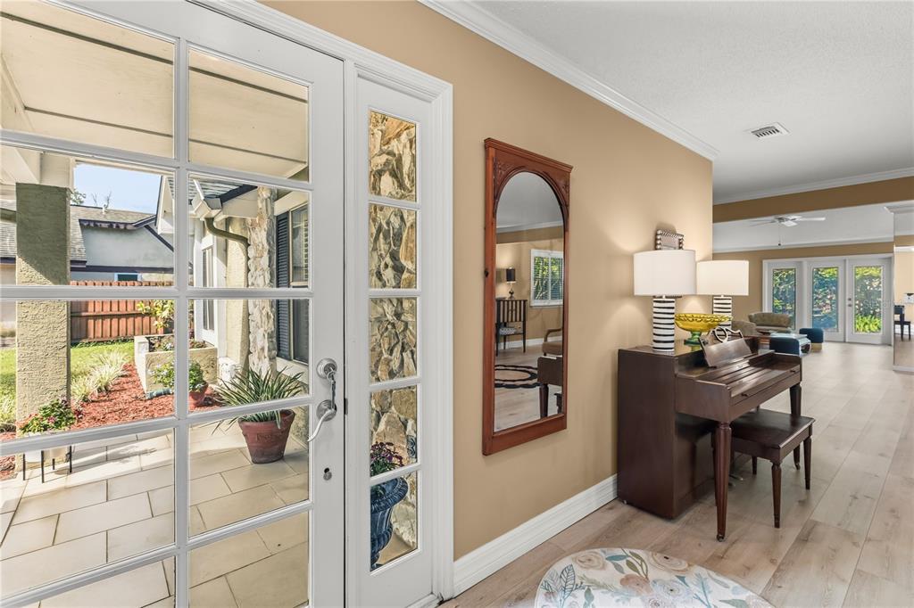 An entryway features a glass-paneled door, a wooden mirror, a piano, and light wood flooring — 3200 HEATHGATE COURT, ORLANDO, FL