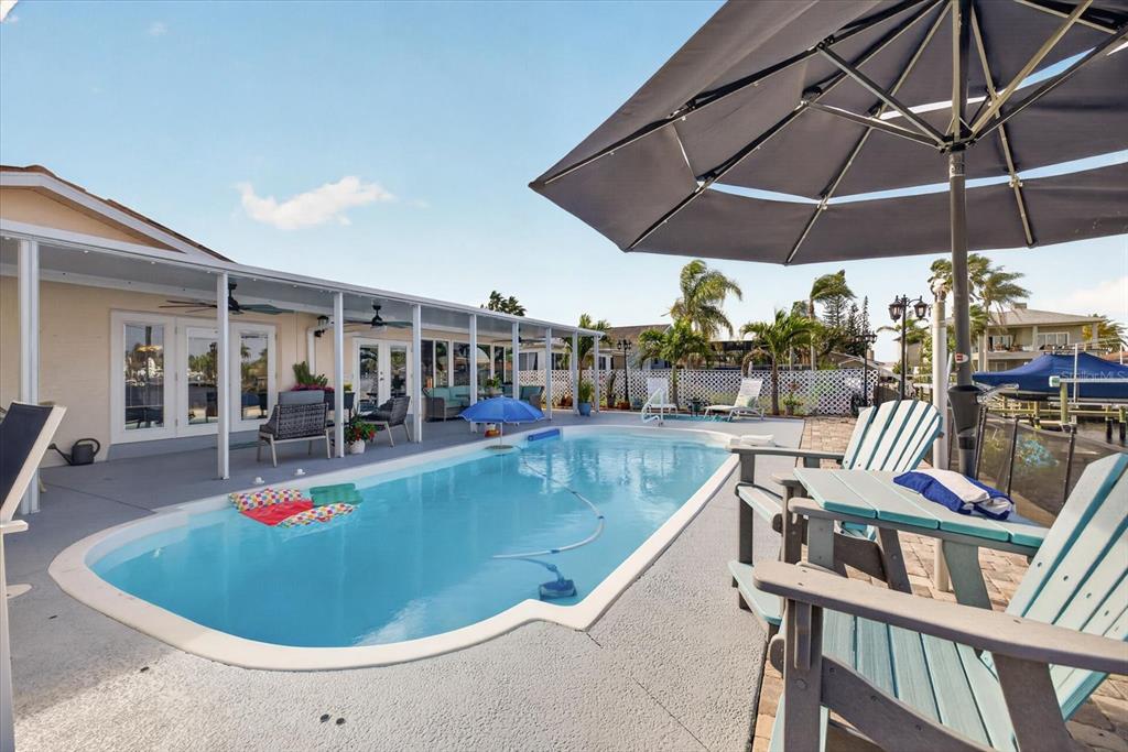 A backyard swimming pool features a covered patio, lounge chairs, and a large patio umbrella — 4969 MARLIN DRIVE, NEW PORT RICHEY, FL