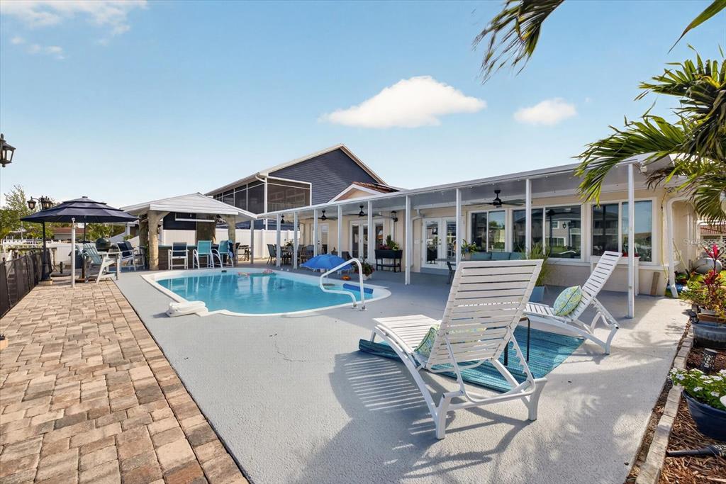 A backyard features a swimming pool, a covered patio, and white lounge chairs — 4969 MARLIN DRIVE, NEW PORT RICHEY, FL