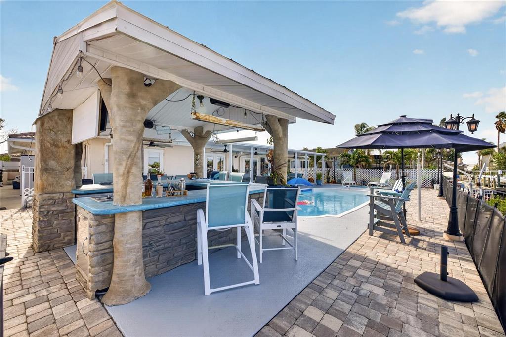 An outdoor covered bar with stone pillars sits on a patio beside a swimming pool — 4969 MARLIN DRIVE, NEW PORT RICHEY, FL