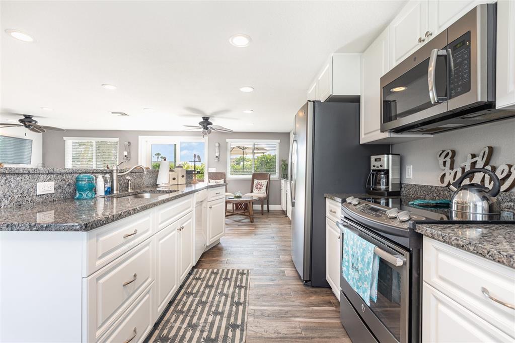 A kitchen features white cabinetry, granite countertops, stainless steel appliances, and wood-look flooring — 3811 101ST STREET W, BRADENTON, FL