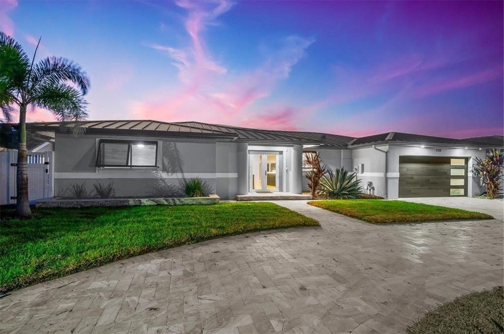 A single-story house with a gray exterior, metal roof, and a paved driveway at sunset — 330 LEEWARD ISLAND, CLEARWATER BEACH, FL