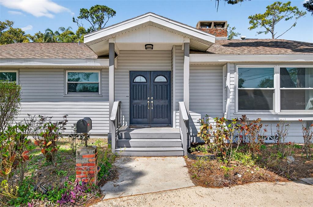 A gray house exterior features a covered entryway with double doors and a brick mailbox — 1520 S KEENE ROAD, CLEARWATER, FL