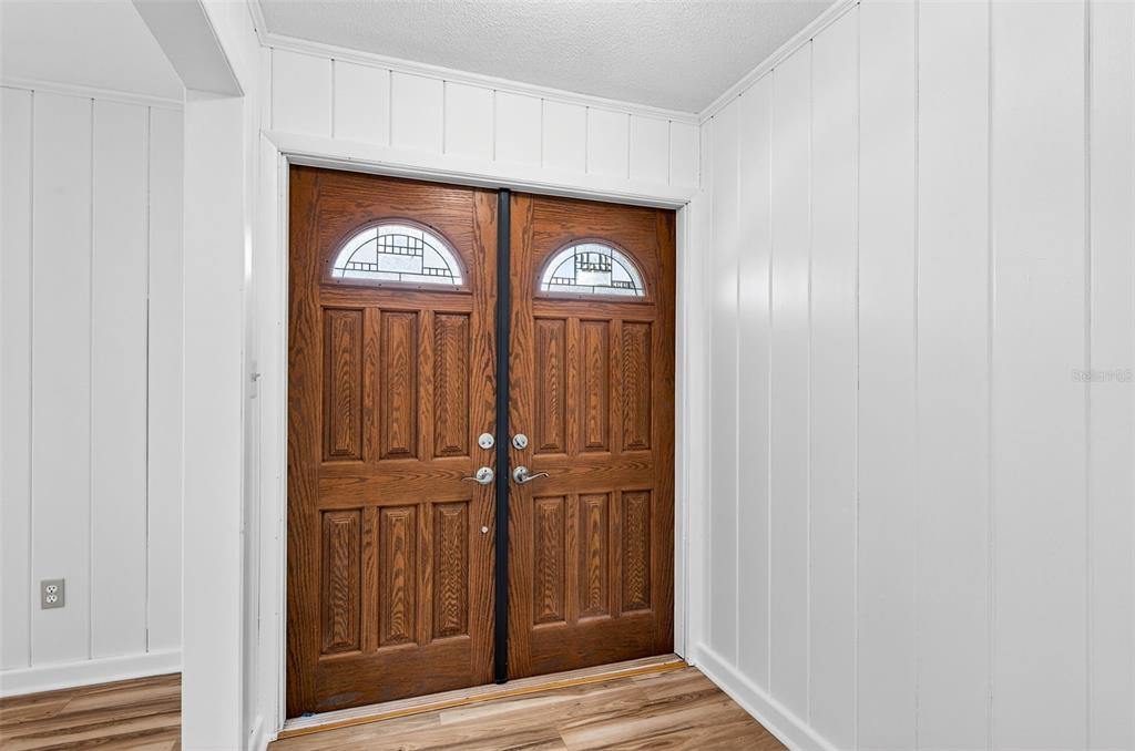 A foyer features white vertical wood paneling, wood-look flooring, and a double wooden front door — 1520 S KEENE ROAD, CLEARWATER, FL