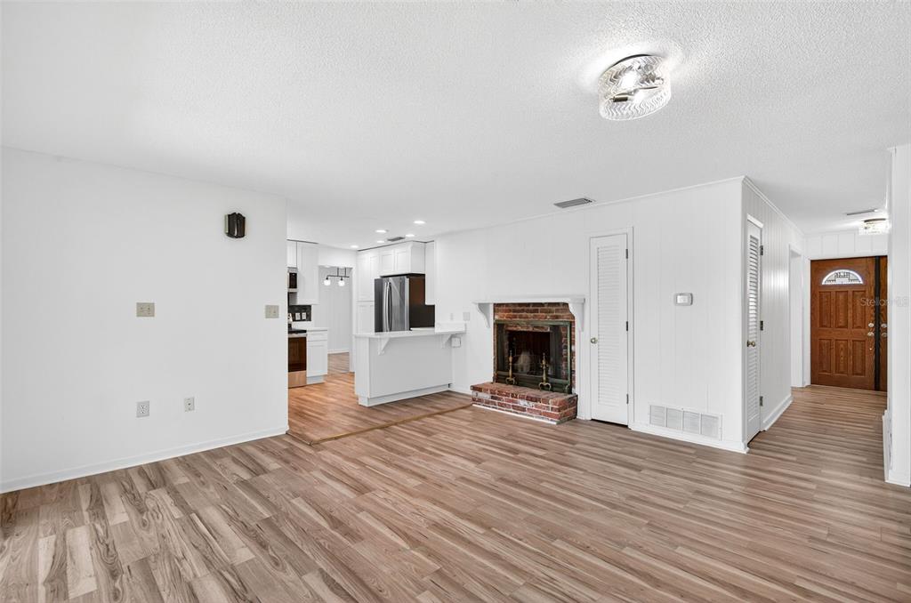 A living room with wood-look flooring, a brick fireplace, and an open kitchen beyond — 1520 S KEENE ROAD, CLEARWATER, FL