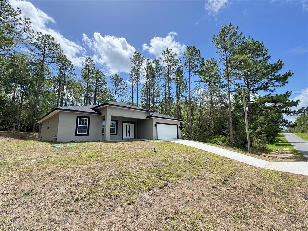 A single-story house with a white garage door and dark trim sits on a grassy lot — 7687 N QUIBBLE AVENUE, DUNNELLON, FL