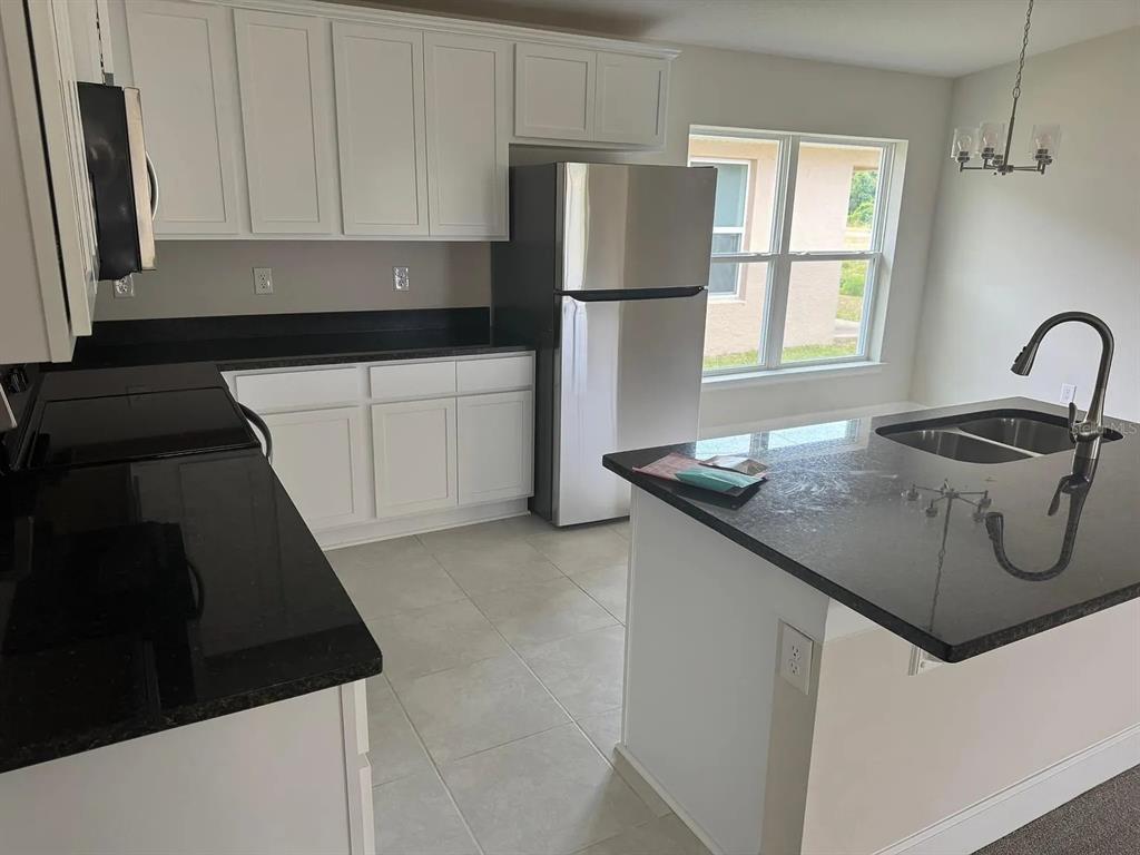 A kitchen features white cabinets, black countertops, stainless steel appliances, and a central island — 3756 SAGEFIELD DR, ST CLOUD, FL