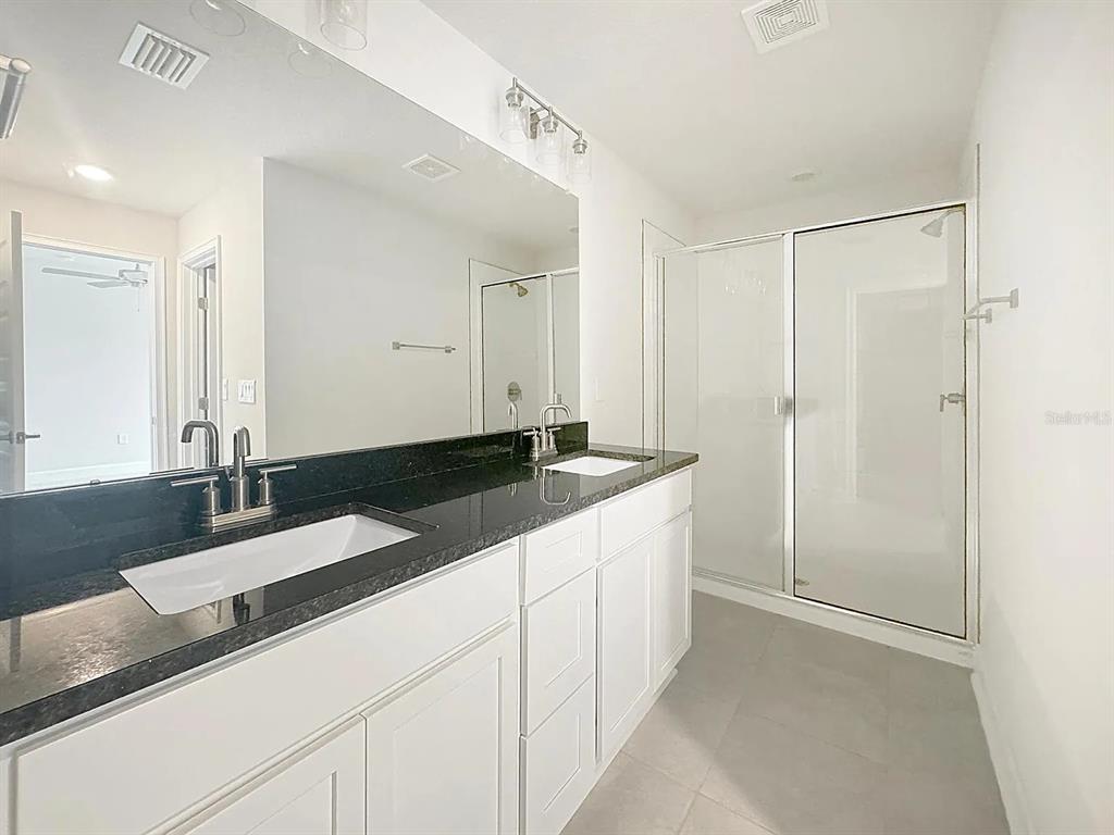 A bathroom features a double vanity with a black countertop and a glass-enclosed shower — 3756 SAGEFIELD DR, ST CLOUD, FL