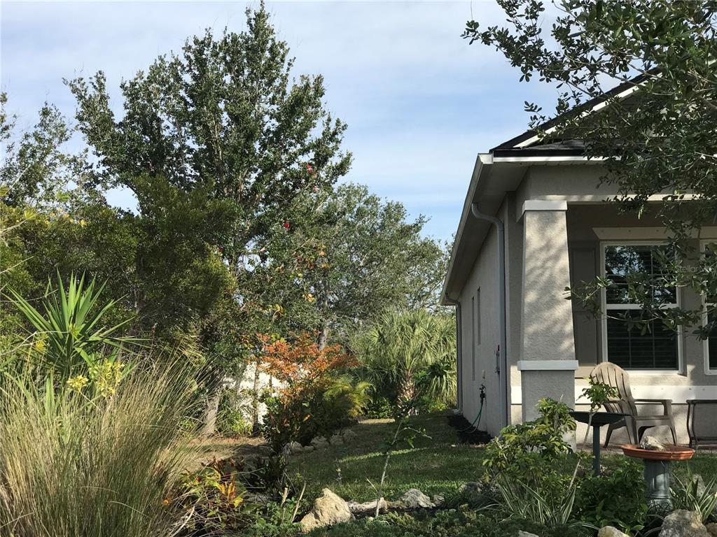 The side exterior of a house features a tan stucco wall, a porch, and landscaping — 15079 WICHITA ROAD, PORT CHARLOTTE, FL