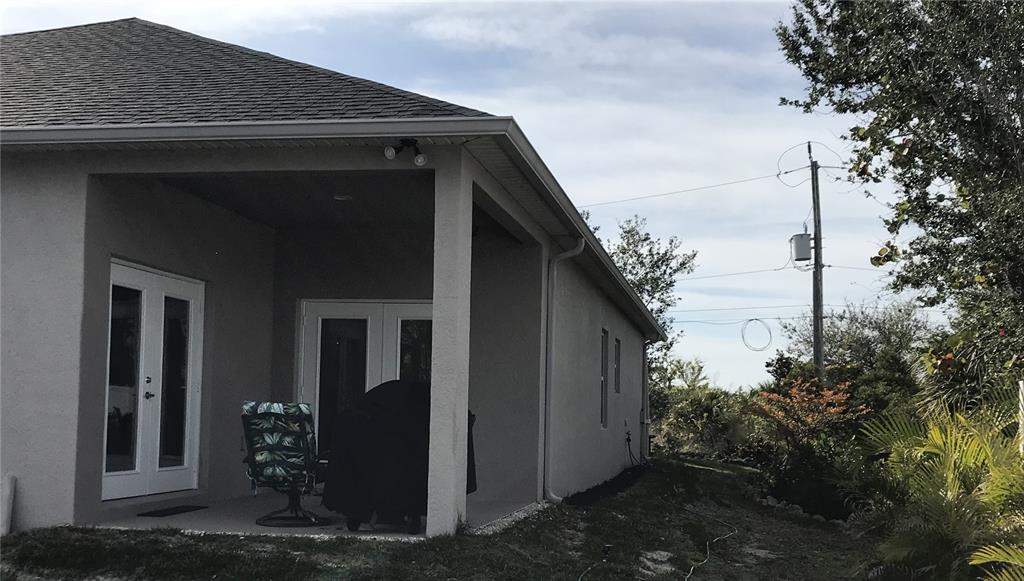 The exterior of a house features a covered patio with two sets of French doors — 15079 WICHITA ROAD, PORT CHARLOTTE, FL