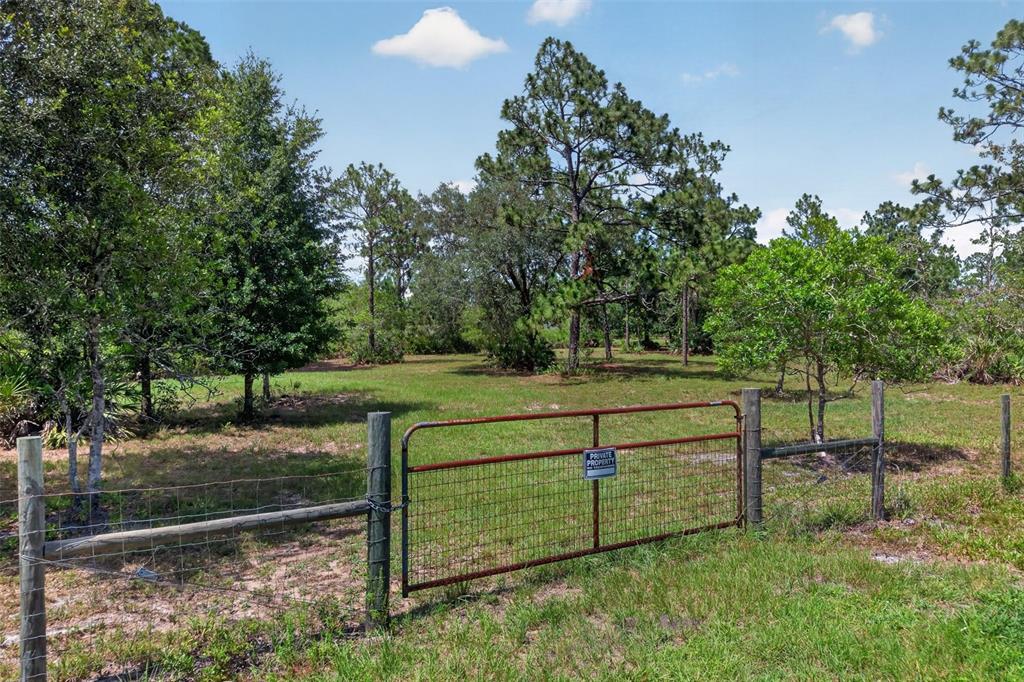 A metal gate and wire fence enclose a grassy lot with scattered trees and shrubs — 20829 QUARTERLY PARKWAY, ORLANDO, FL