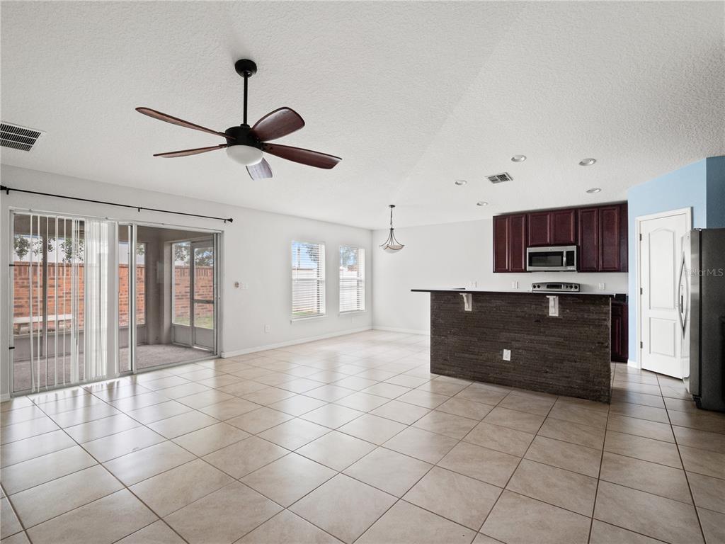 An open-concept kitchen and living area features tile flooring, a dark stone breakfast bar, and sliding doors — 411 MILLWOOD PLACE, WINTER GARDEN, FL
