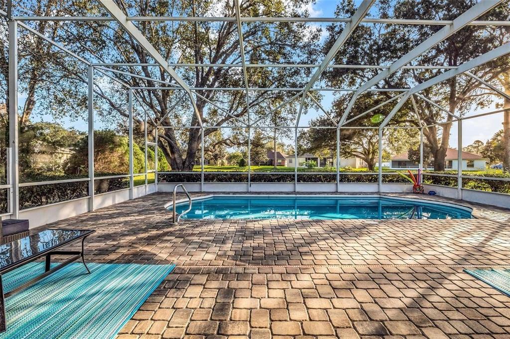 A screened-in patio features a swimming pool, paver flooring, and mature trees in the background — 9 MOUNT VERNON LANE, PALM COAST, FL