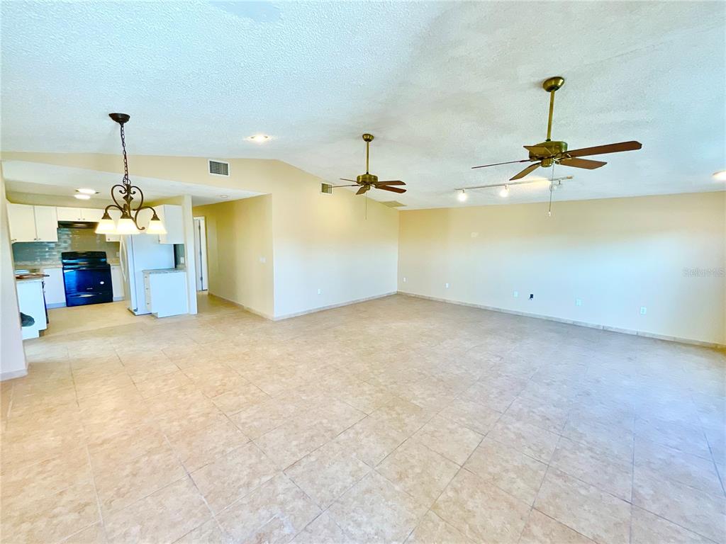 A large, open-concept living area features beige tile flooring, two ceiling fans, and a kitchen — 3127 CORONA DRIVE, HOLIDAY, FL