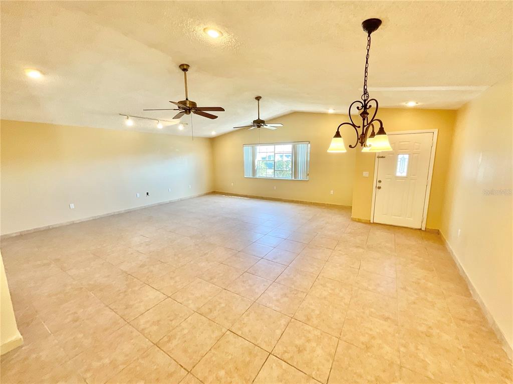 A spacious living room features light-colored tile flooring, two ceiling fans, and a chandelier — 3127 CORONA DRIVE, HOLIDAY, FL