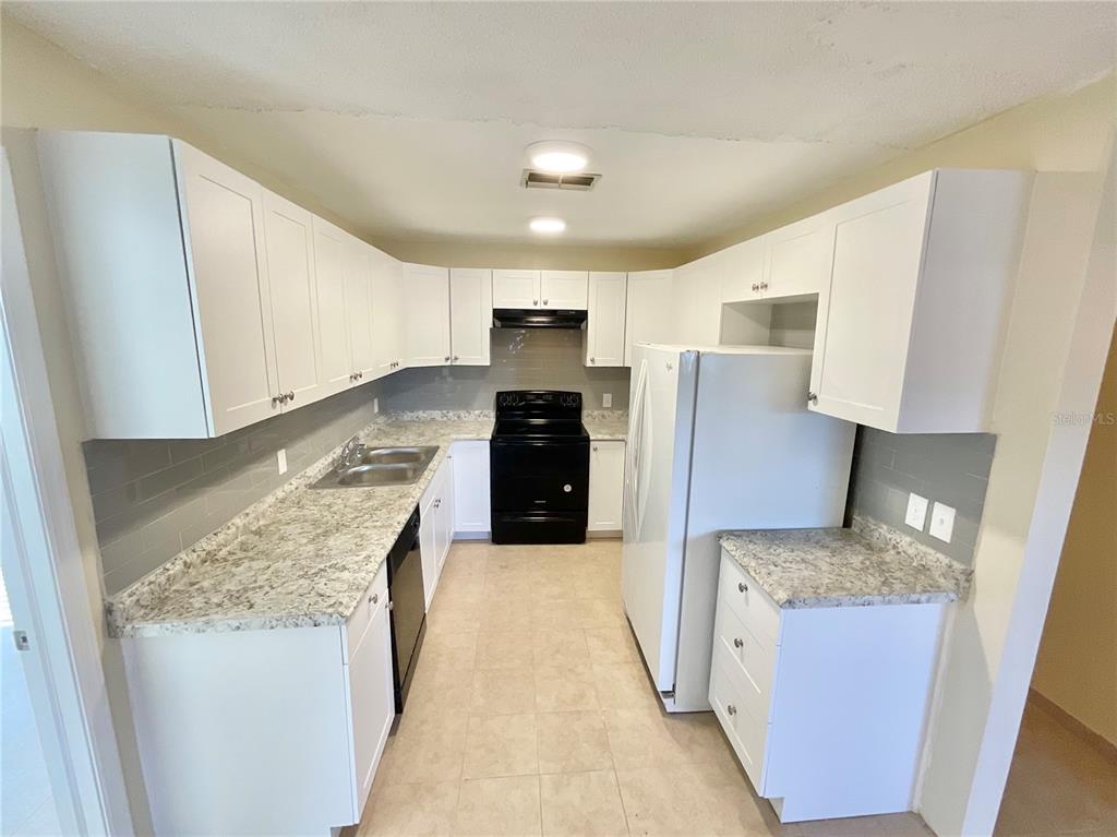 A kitchen features white cabinets, granite-look countertops, a gray tile backsplash, and black appliances — 3127 CORONA DRIVE, HOLIDAY, FL
