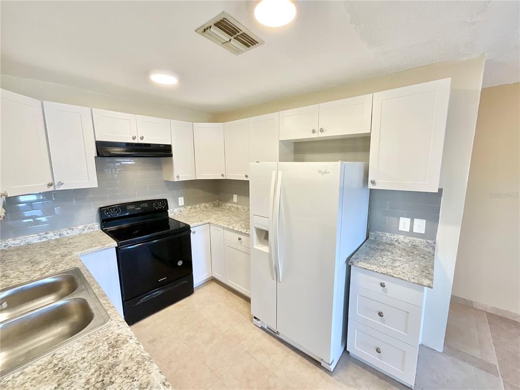 A kitchen features white cabinets, granite countertops, a black stove, and a white refrigerator — 3127 CORONA DRIVE, HOLIDAY, FL