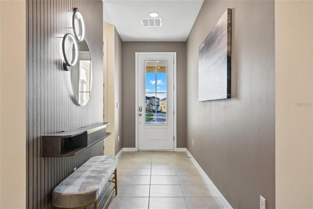 A bright entryway features a tiled floor, a modern wall-mounted shelf, and a front door — 8905 COCONUT BREEZE DRIVE, KISSIMMEE, FL