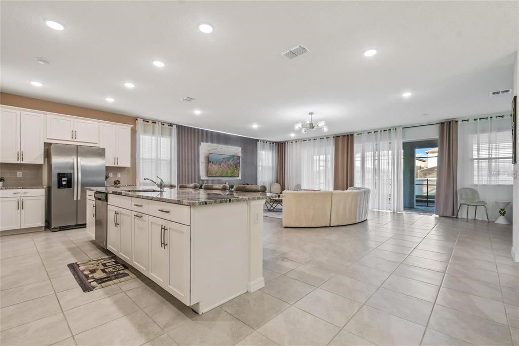 A kitchen with white cabinets and a large island opens into a spacious living area — 8905 COCONUT BREEZE DRIVE, KISSIMMEE, FL