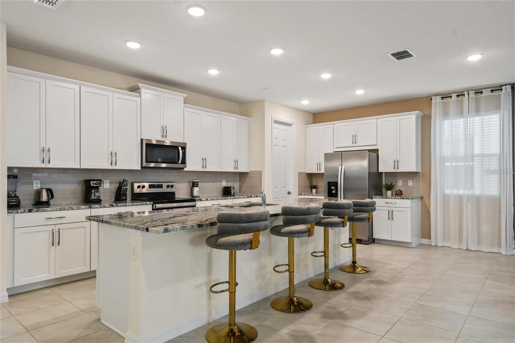 A kitchen features white cabinets, stainless steel appliances, a granite island, and four bar stools — 8905 COCONUT BREEZE DRIVE, KISSIMMEE, FL