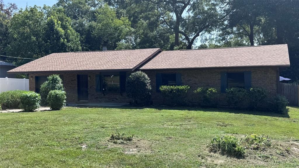 A single-story brick house with a brown shingled roof sits behind a grassy lawn — 3315 NE 31ST AVENUE, OCALA, FL