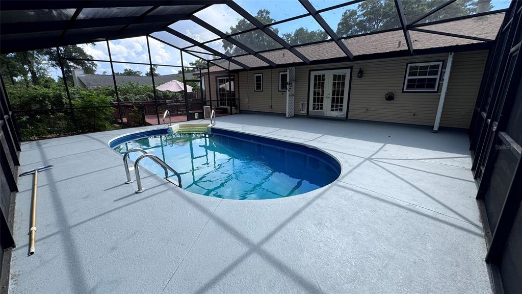 An oval swimming pool sits on a gray deck inside a screened-in patio enclosure — 3315 NE 31ST AVENUE, OCALA, FL