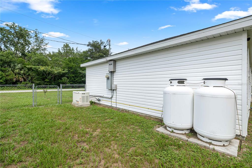 The exterior side of a white house features two propane tanks and a backup generator — 94 WILLOW ROAD, OCALA, FL