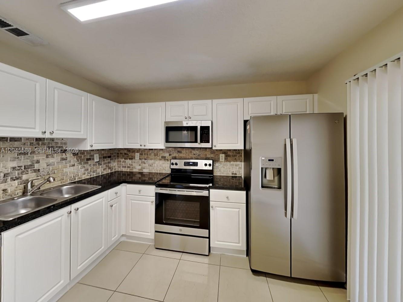 A kitchen features white cabinets, stainless steel appliances, and a brown tiled backsplash — MIAMI, FL