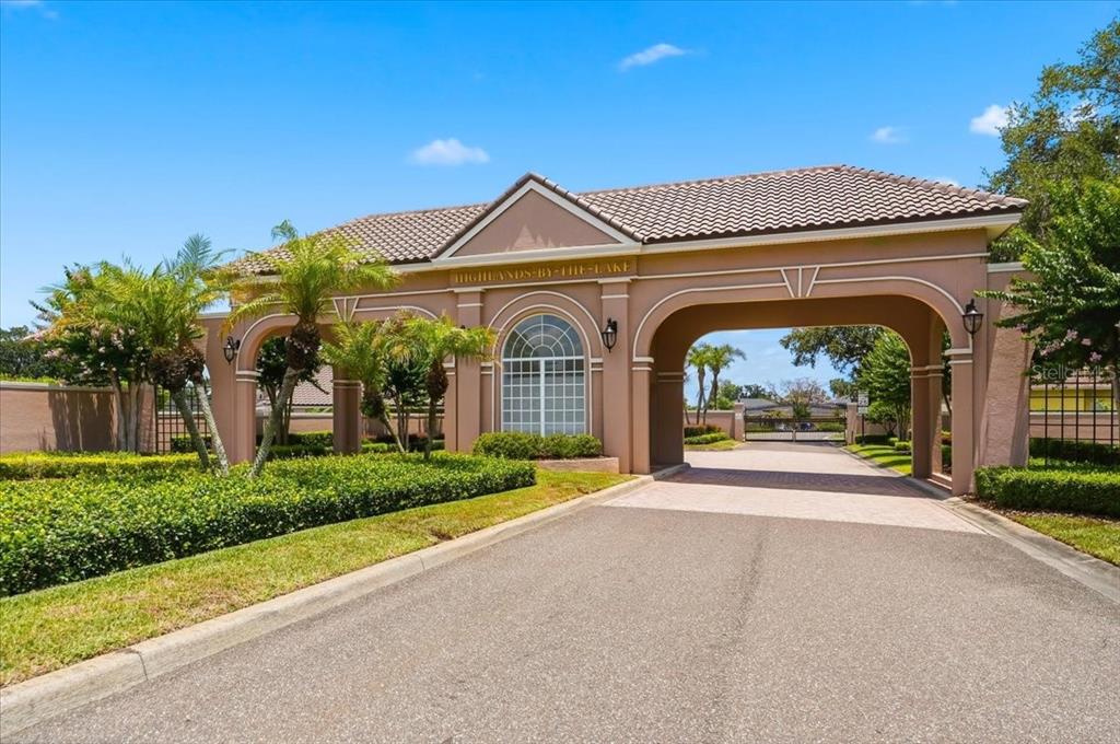 The entrance to the Highlands-by-the-Lake community features a tan stucco gatehouse with arched openings — 5112 HIGHLANDS LAKEVIEW LOOP, LAKELAND, FL