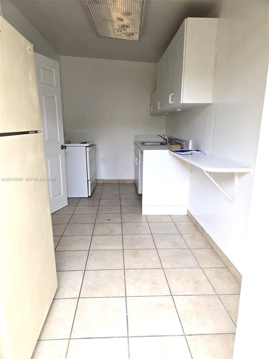 This kitchen features white cabinets, tile flooring, a sink, and a white stove — 4610 SW 40th St # 1, West Park FL 33023, WEST PARK, FL